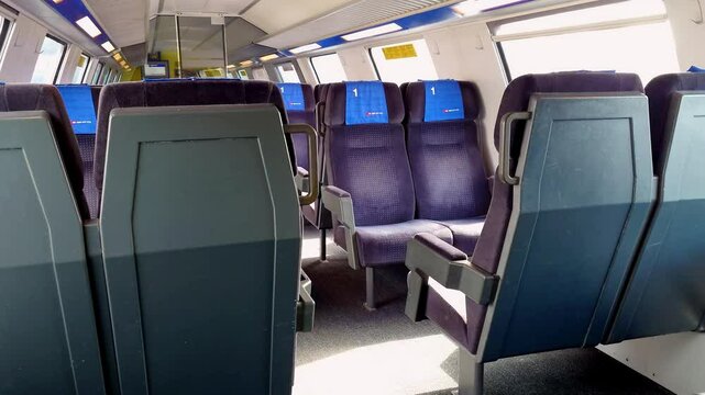Empty first class bench seats inside moving public passenger train in Europe. Wide angle view, large windows, green summer nature landscape outside, real time, no people