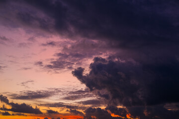 Dramatic sunset sky with vibrant orange, pink, and purple hues blending into dark clouds over a city skyline, creating a stunning contrast between light and shadow in the evening atmosphere.
