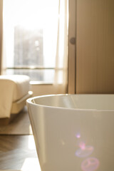 Close up of luxurious freestanding bathtub with a blurred modern hotel room in background during sunset. Sunlight effect. Lifestyle interior