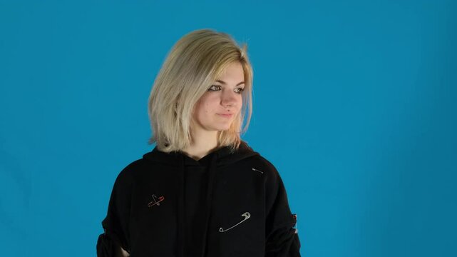 Blonde girl looks away with frustrated expression on blue background. Young woman body language reflecting dissatisfaction with situation