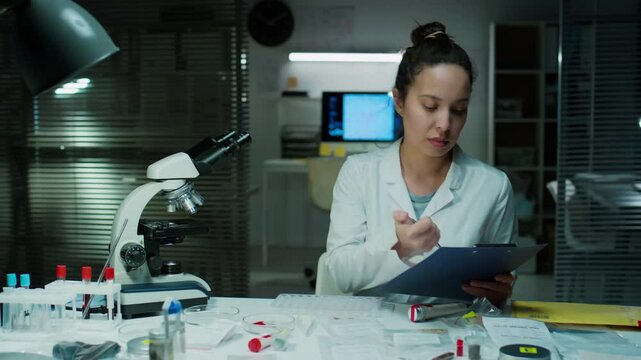 Female forensic scientist analysing bullet in evidence bag and taking notes while working in crime laboratory