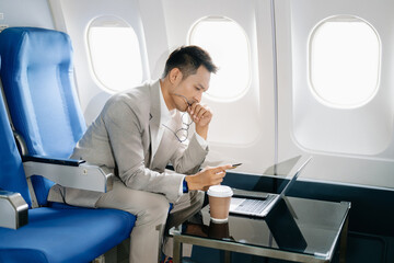 Fototapeta premium frustrated man sitting on an airplane with her head in her hands. Asian Businessman sitting in airplane working laptop and tablet