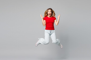 Fototapeta premium Full body young surprised shocked excited fun happy woman she wear red t-shirt casual clothes jump high look camera spread hands isolated on plain grey background studio portrait. Lifestyle concept.