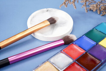 brushes on coaster with face painting palette on blue background