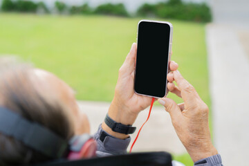 Back view of excited senior man with headphones and cell phone in the city park on the sunny day.