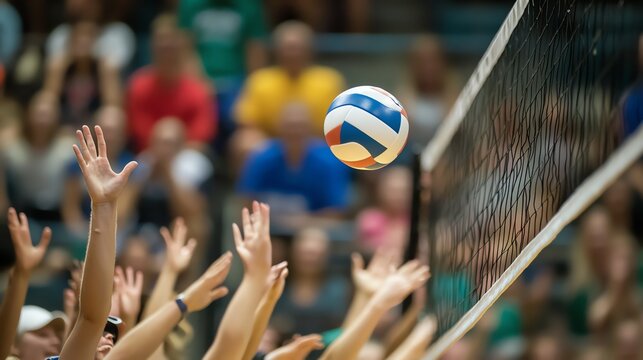 A volleyball flies toward the net as players on the court reach for it.