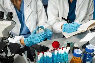 Chemist scientist holding test tube and tablet conducting experiment in laboratory with equipment,...