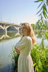beautiful young artist in a white dress among the trees on the river bank