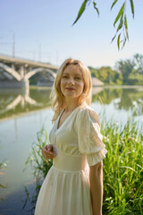 beautiful young artist in a white dress among the trees on the river bank