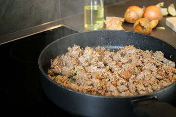 Close up cooked ground beef meat frying in a pan in the kitchen, blurry background with onions and oil spray 