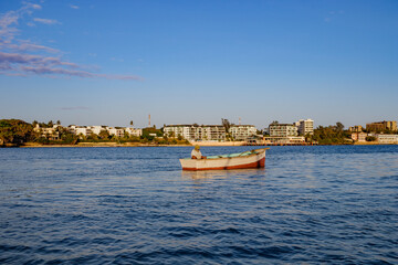 A fisherman in a boat in the ocean with the cityscape behind him