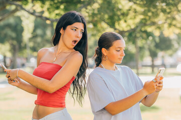 girl with phone spying on her friend's mobile phone or smartphone