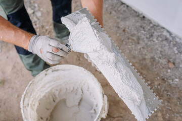 Close-up of a worker applying plaster to a trowel from a bucket, preparing for wall plastering....