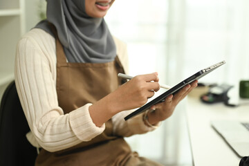 Smiling young muslim woman wearing hijab checking order on digital tablet. E-commerce and small business concept