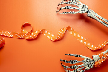 A skeleton hand with an orange ribbon with a white polka dot design. The skeleton is positioned on...