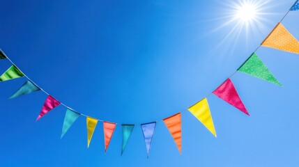 Colorful pennant flags strung against a bright blue sky with the sun shining overhead.