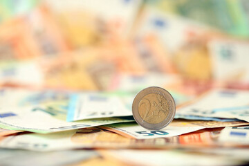Two euro coin lies on huge amount of different euro dollars banknotes