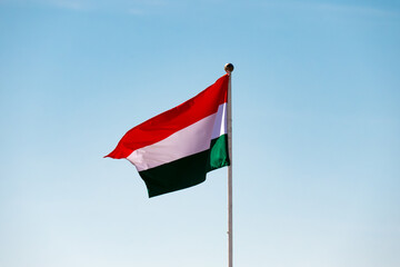 The flag of Hungary is flying against a clear blue sky, symbolizing patriotism and national identity