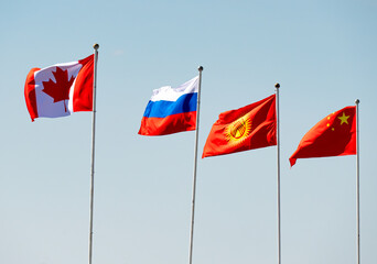 Flags of Canada, Russia, Kyrgyzstan, and China flying together against a clear blue sky, symbolizing international cooperation and diplomacy