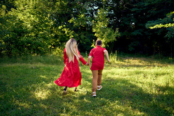 Fototapeta premium mother and preteen son in red clothes are circling and running in the garden