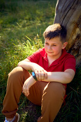 preteen boy in a red t-shirt is sad near a withered tree in the park