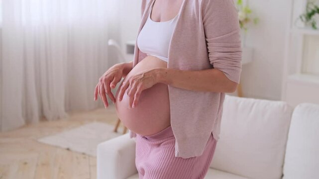 Close up of a Caucasian middle aged pregnant woman fondle rounded belly relaxing at home. Concept of a baby expecting and protection.