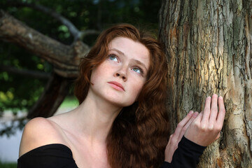 Naklejka premium Sensual close up outdoor portrait of sad ginger caucasian attractive girl with red hair and freckles near the tree