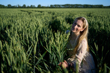 portrait of a young blonde woman in a pastel chiffon dress in a green wheat field