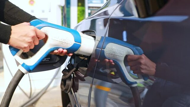 Young woman's hand driving an EV car is safely closing the charging plug and cover of her EV car inside gas station after charging is complete.