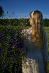 portrait of a young blonde woman in a pastel chiffon dress walking with a giant bouquet of wild...