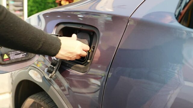Young woman's hand driving an EV car is safely closing the charging plug and cover of her EV car inside gas station after charging is complete.