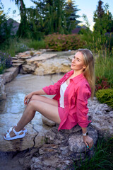 portrait of a young blonde woman in hot pink shorts and shirt near an artificial waterfall