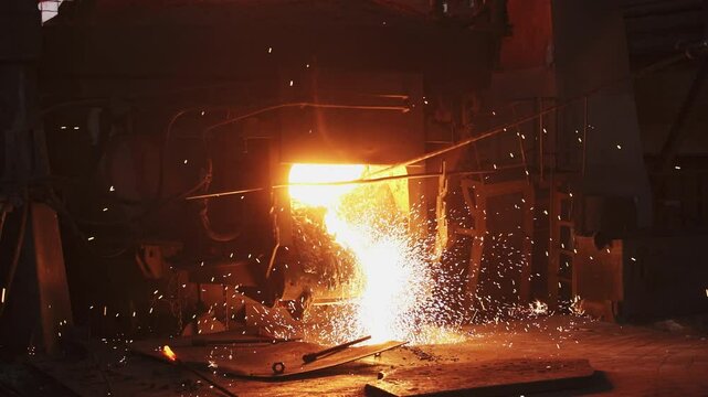 Molten metal is being poured out, producing bright sparks within a vibrant foundry environment. Stock Clip