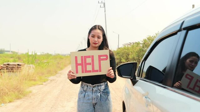 Asian woman standing next to car holding sign saying HELP asking for help Electric car battery dead in remote area : Problems using EV while traveling concept.