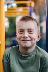 Obraz premium A school-age boy in a green T-shirt spends time on horizontal bars, a playground in sunny weather. Front view