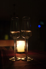 There are two beautiful wine glasses elegantly placed on a table, with a soft, flickering candle glowing gently in the background
