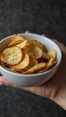 Bowl of crispy potato chips held in hand.