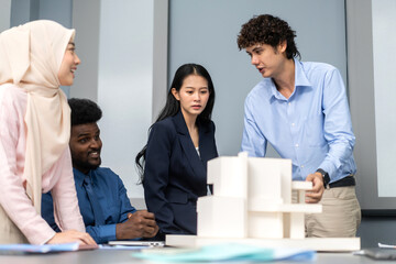 Architects engineers collaborating on building design project in modern office, diverse team of professionals female muslim architect and male engineers discussing architectural model of structure