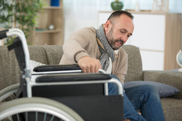 Fototapeta premium disabled man tries to move from sofa to wheelchair