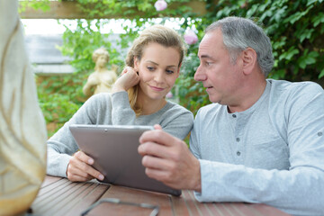 Fototapeta premium father and adult daughter sat outdoors looking at tablet