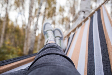 Outdoor recreation. Women's legs, shod in sneakers, in a hammock in the autumn forest. The concept...