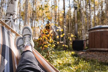 Outdoor recreation. Women's legs, shod in sneakers, in a hammock in the autumn forest. The concept of a cozy autumn vacation.