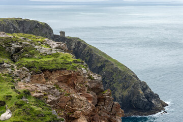 Two sheep shelter in a grassy hollow from the strong Atlantic wind, with rocky cliffs and Carrigan...