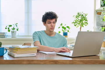 Young male college student sitting at desk at home typing on laptop