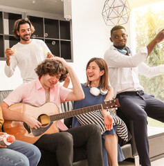 A group of multiracial teenagers is playing guitar and singing a song together while happily having fun blowing bubbles at the afternoon party. Recreational activity and celebration concepts.