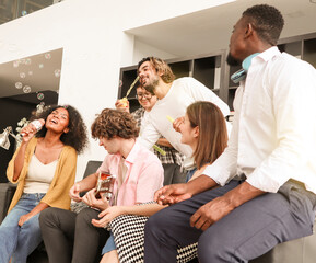 A group of multiracial teenagers is playing guitar and singing a song together while happily having fun blowing bubbles at the afternoon party. Recreational activity and celebration concepts.