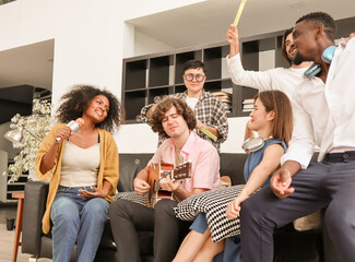 A group of multiracial teenagers is playing guitar and singing a song together while happily having fun blowing bubbles at the afternoon party. Recreational activity and celebration concepts.