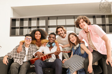 A group of multiracial teenagers playing guitar and singing a song together at an afternoon party. A group of Millennials sitting and spending time together on the holiday weekend..