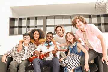 A group of multiracial teenagers playing guitar and singing a song together at an afternoon party. A group of Millennials sitting and spending time together on the holiday weekend..