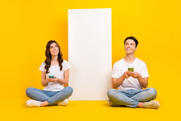 Full length photo of positive dreamy husband wife dressed white t-shirts typing sms device empty space isolated yellow color background